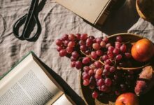 Stylish flat lay featuring wine, fruits, and books on a textured surface in warm sunlight.